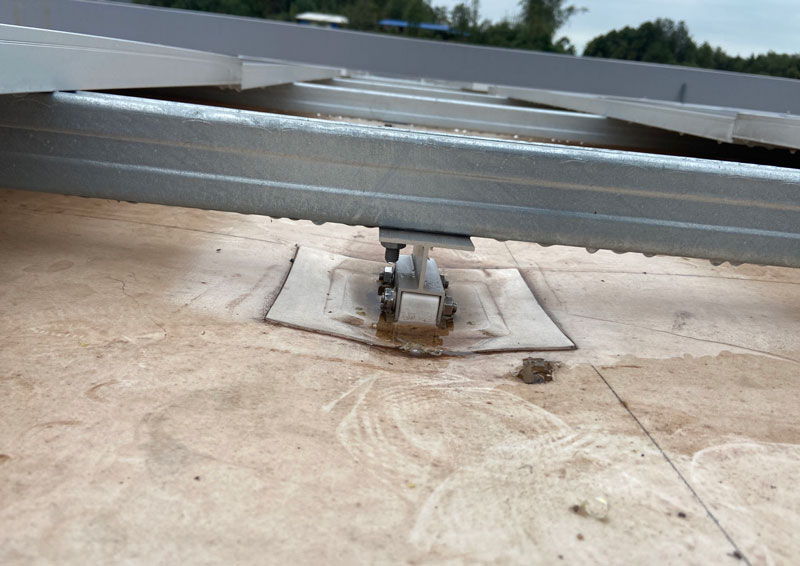 Low-angle view of a rooftop solar mounting rail system secured to a flat concrete roof with metal clamps fansing the structure.